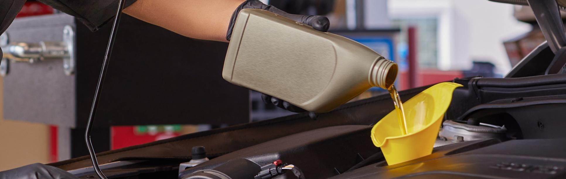Auto service technician replacing motor oil in a vehicle through a funnel